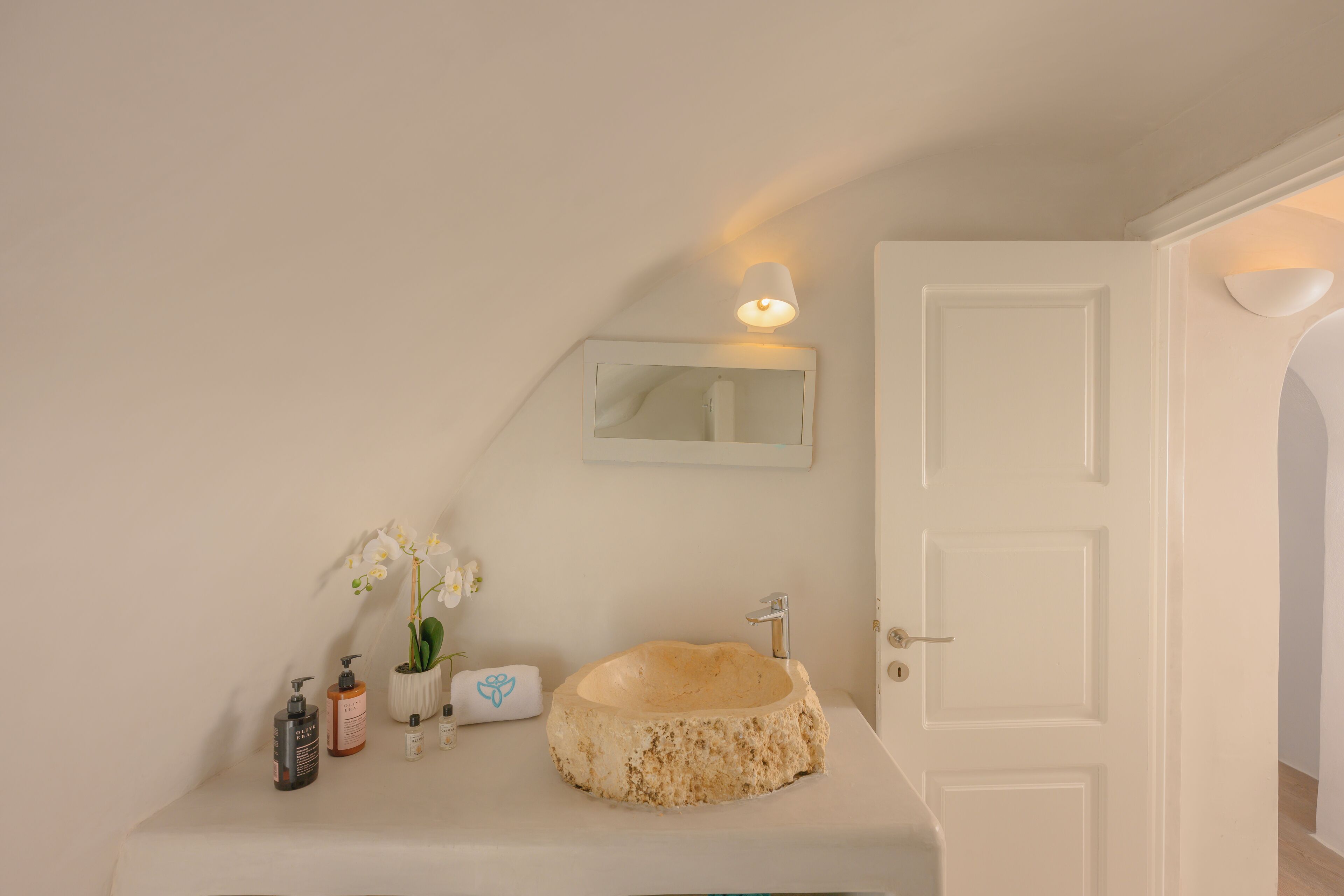Een badkamer met een stenen wastafel, witte wanden, een spiegel en een deur.