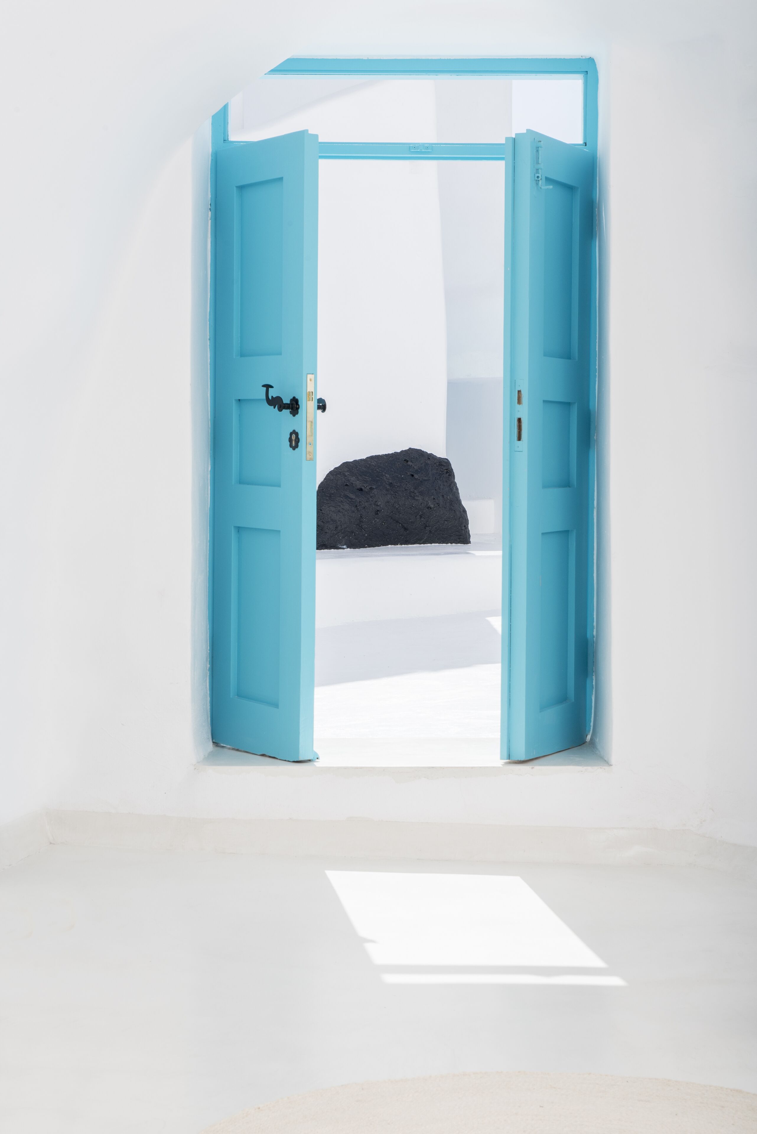 Une pièce avec une porte bleue, un mur blanc et un objet noir posé sur une surface blanche.