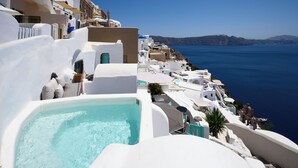 A white-washed building with a pool, overlooking a coastal area with clear blue waters and distant hills. - Sophia Oia View (Santorini)