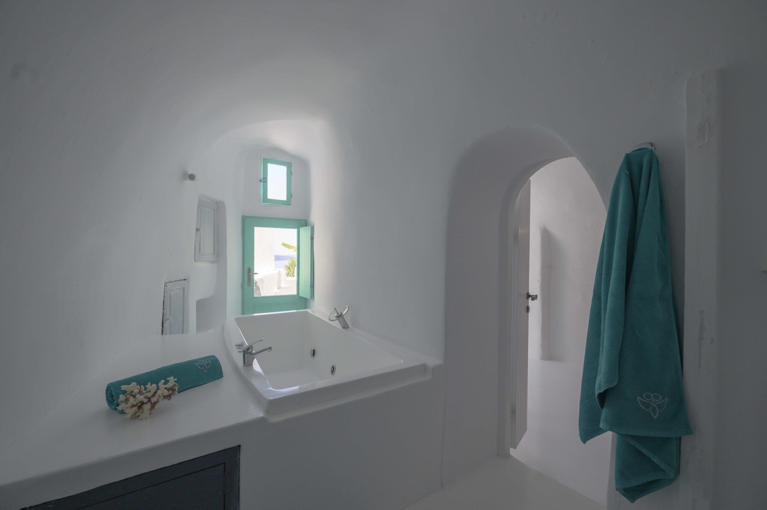 Un baño con un lavamanos blanco, una ventana con marco verde y una toalla verde azulada colgada en la pared.