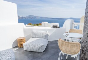 A terrace with a white-walled room, a round table, wicker chairs, and a patterned cushion. - Sophia Oia View (Santorini)