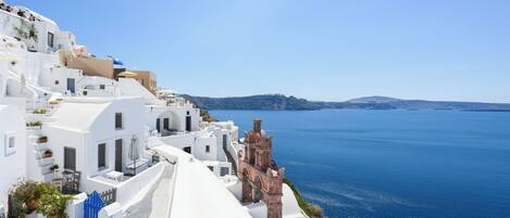 A coastal building with white walls and a red-roofed structure, overlooking a clear blue sea.