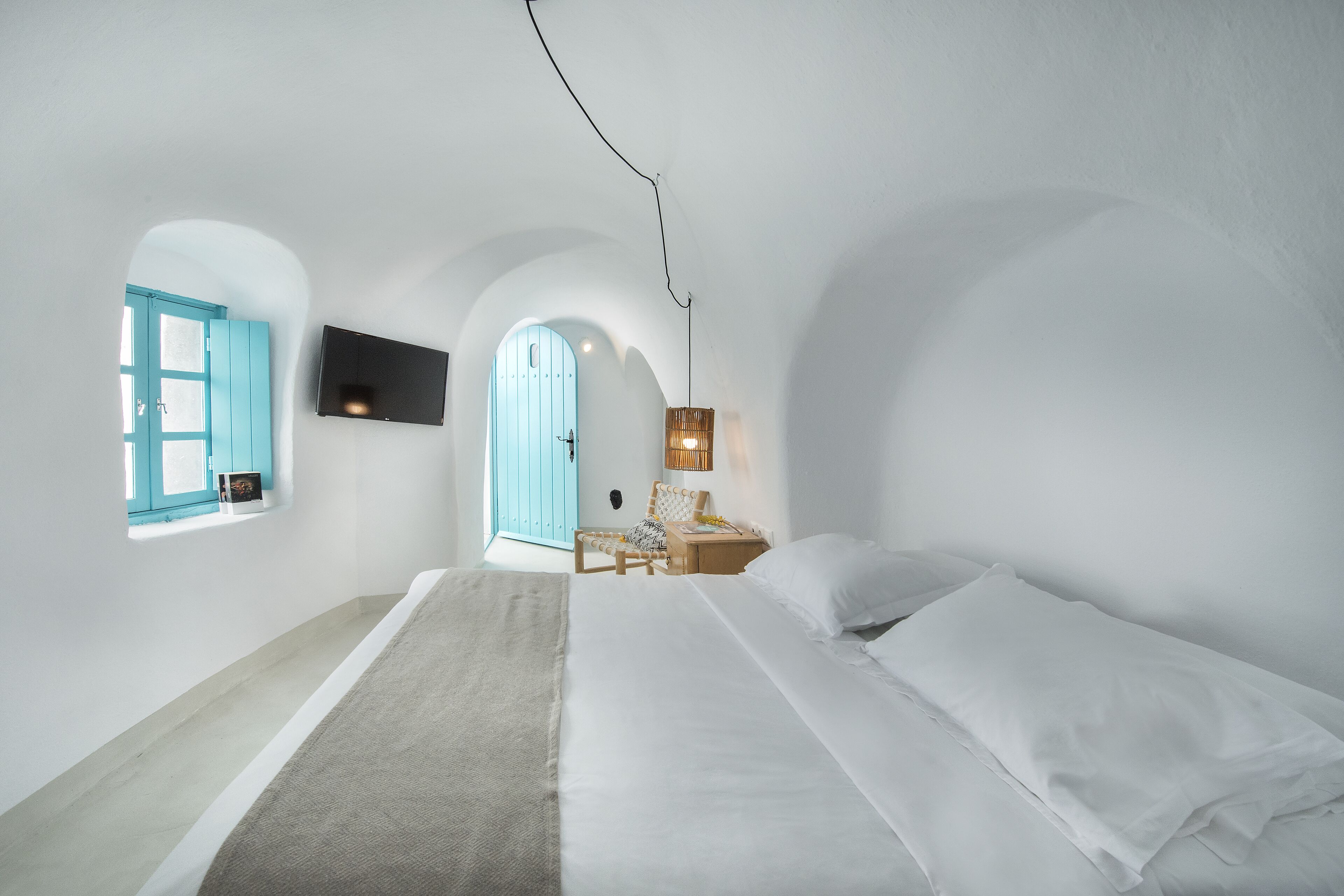 A bedroom with a large bed, a chair, a small table, a TV, and a window with a view of the outside.