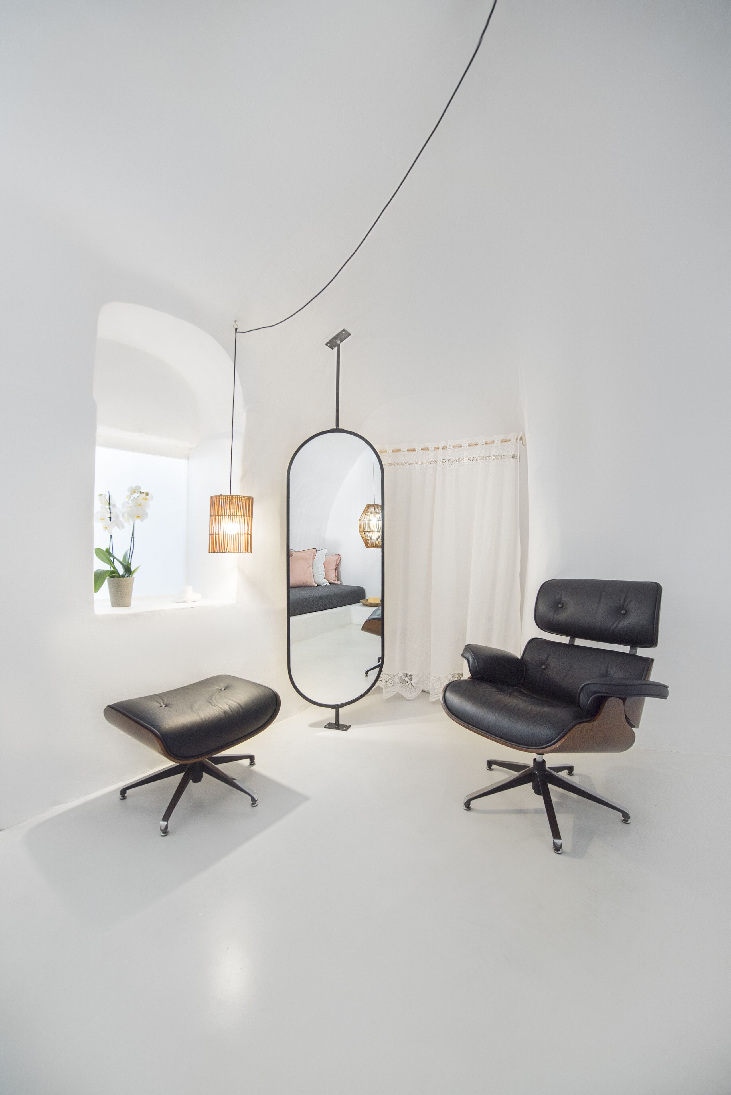 Een minimalistische kamer met een grote spiegel, twee zwarte bureaustoelen, een hanglamp en een raam met witte gordijnen.