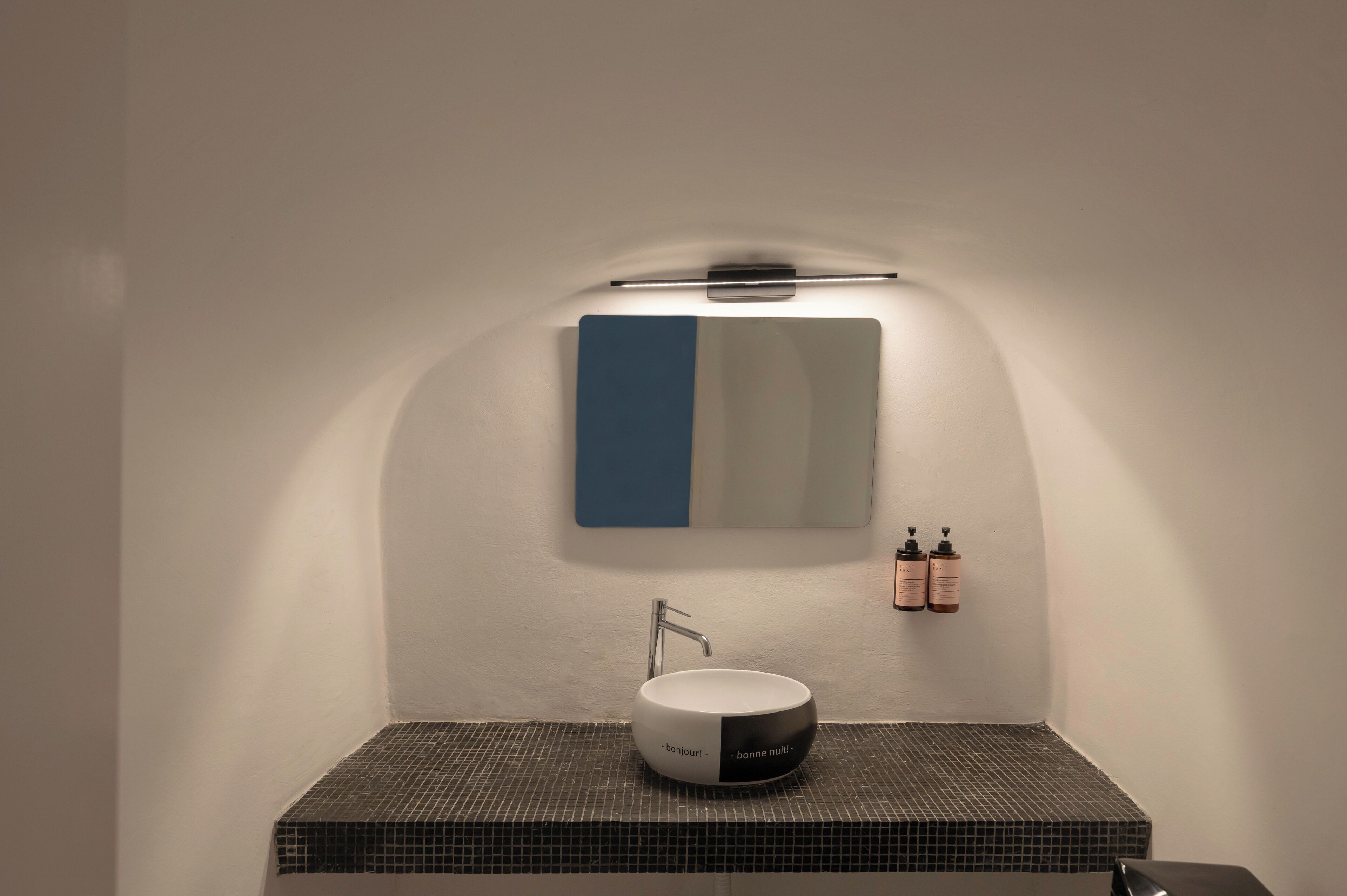 Un baño moderno con un lavamanos blanco, un espejo azul y blanco y dos botellas de artículos de aseo en la pared.