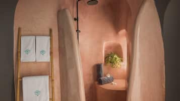 Un baño con una escalera de madera, dos toallas con diseño de hojas, una zona de ducha con una planta y una toalla sobre un estante.