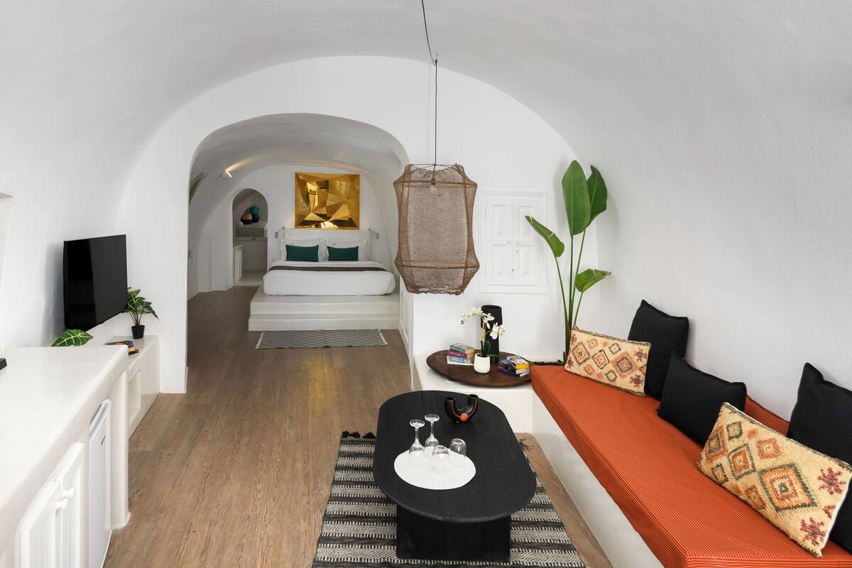 Una sala moderna con un sofá, una mesa de centro y un comedor. Hay una zona de cocina con una cafetera y un televisor.