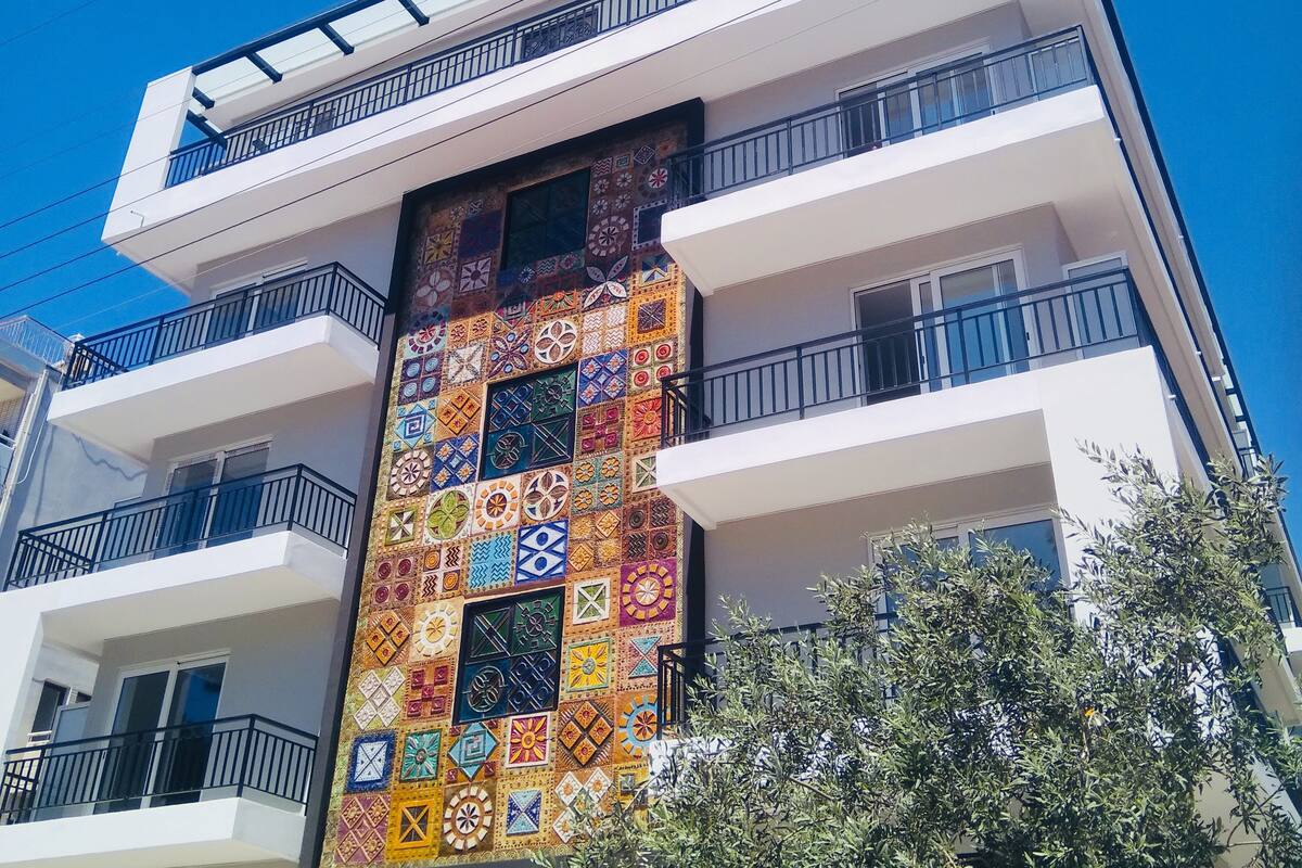 A multi-story building with balconies, a patterned facade, and a clear blue sky.