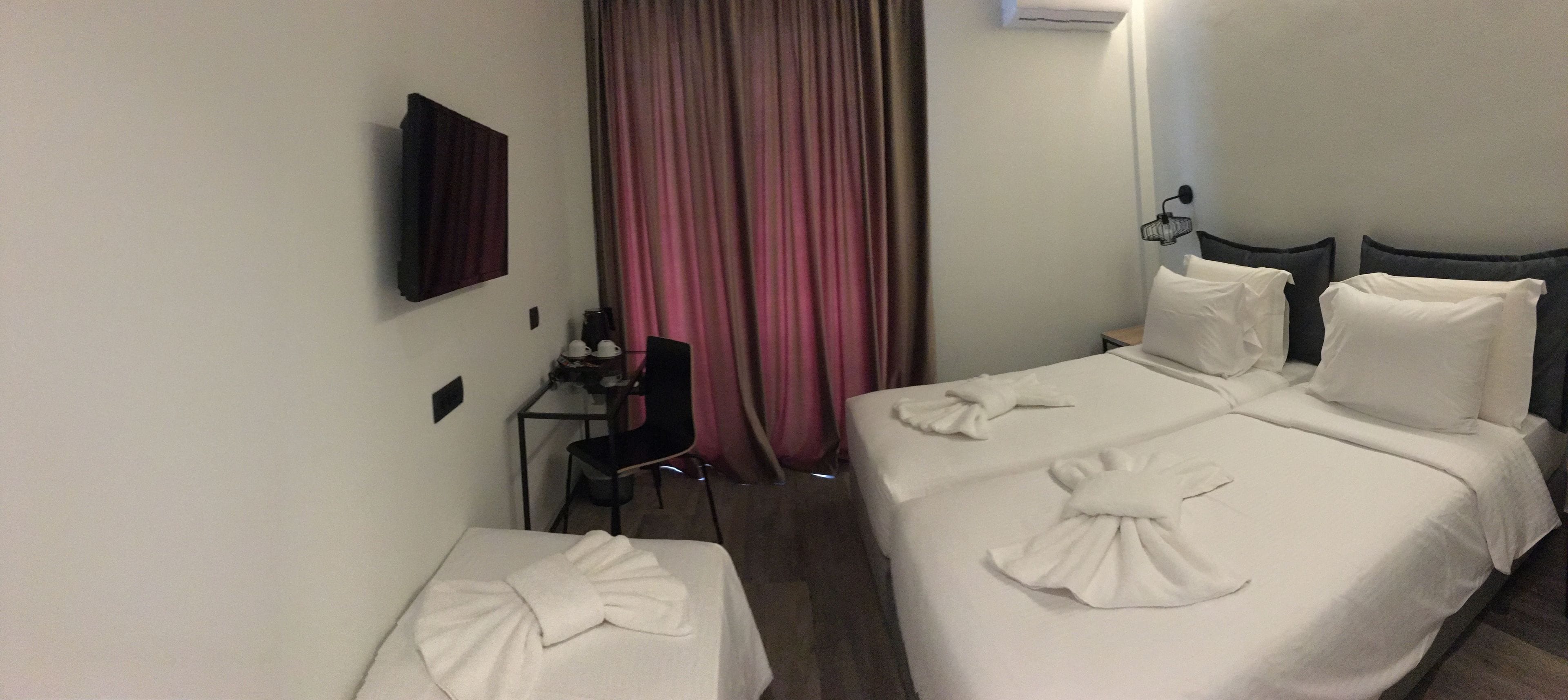 Habitación de hotel con dos camas, un escritorio, una silla y un televisor en la pared.