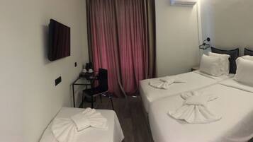 Quarto de hotel com duas camas, uma escrivaninha, uma cadeira e uma televisão na parede.