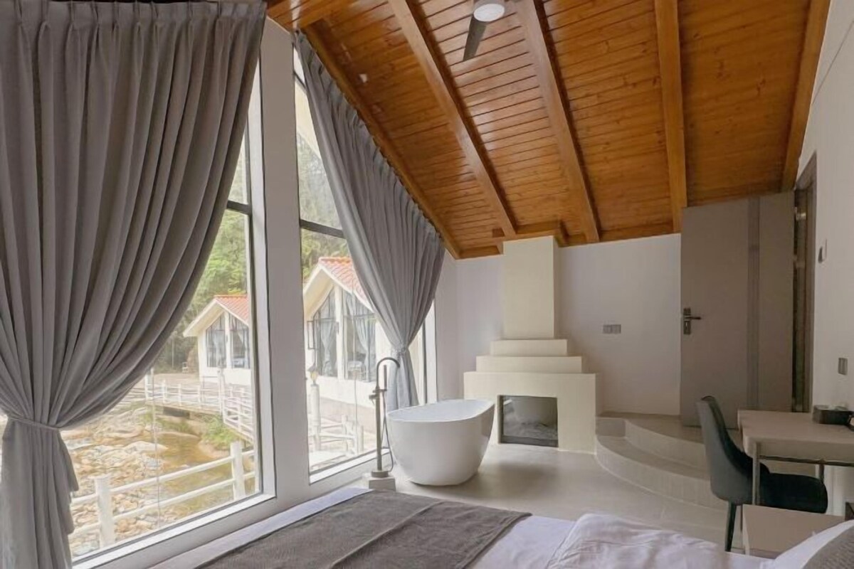 Un dormitorio con un ventanal grande, una bañera, una cama y techo de madera.