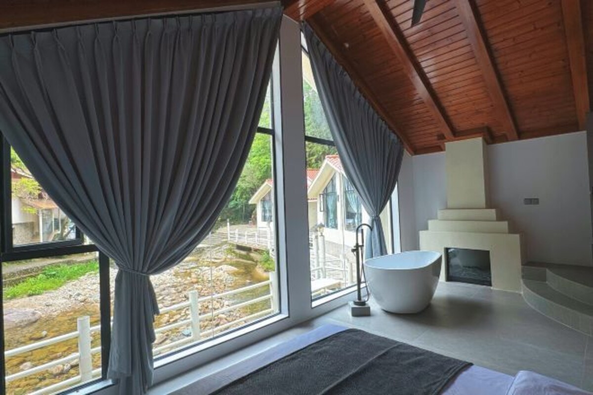 Un baño moderno con un ventanal grande, una bañera y una chimenea de piedra.