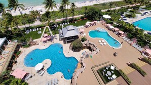An aerial view of a resort with multiple swimming pools, sun loungers, and palm trees. - Magnificent Modern Direct Oceanfront 3 Bedroom - 1401 (Miami Beach)