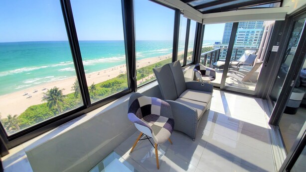 A balcony with a view of the beach and ocean. There is a sofa and a chair. - Magnificent Modern Direct Oceanfront 3 Bedroom - 1401 (Miami Beach)