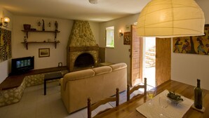 A cozy living room with a stone fireplace, a sofa, a dining table with a bottle of wine, and a television.