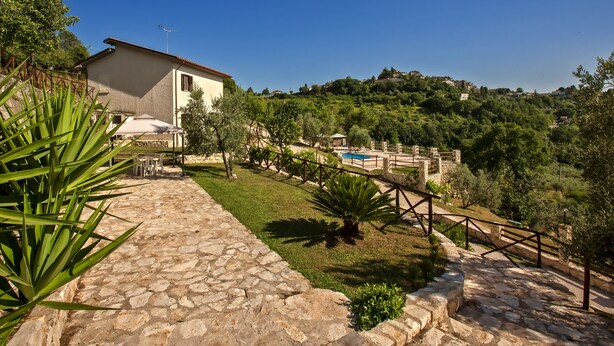 A stone pathway leading to a house with a pool, surrounded by greenery and hills.