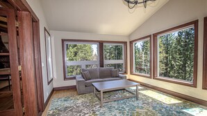 A room with a sofa, a coffee table, and large windows offering a view of trees. - Highlands Lodge by Hauserman Rental Group (Tahoe City)