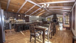 A spacious kitchen with wooden beams, a stone fireplace, and a large dining area with multiple chairs. - Highlands Lodge by Hauserman Rental Group (Tahoe City)