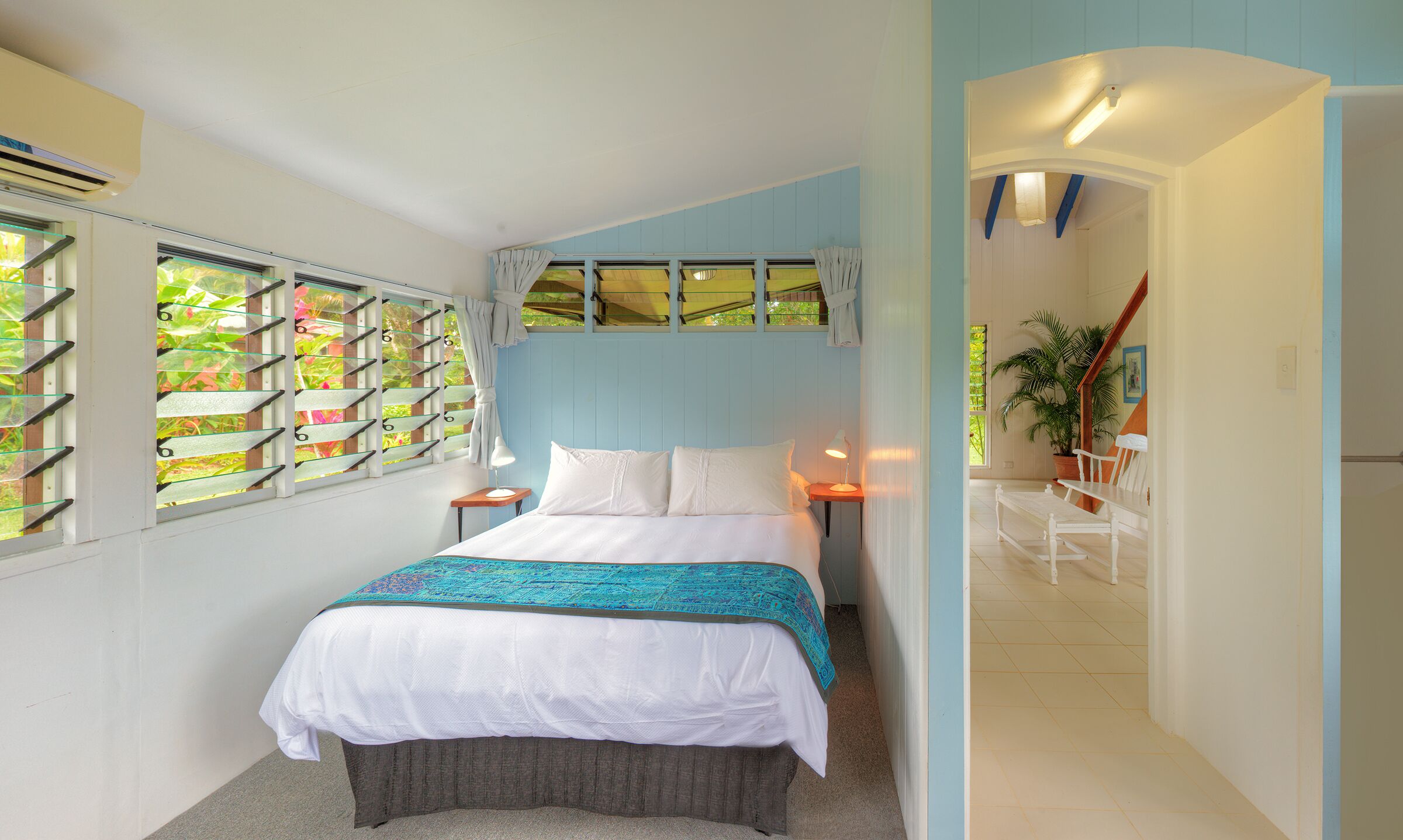 Une chambre à coucher comprenant un lit, deux tables de chevet, une fenêtre donnant sur un espace verdoyant et une porte menant à une autre pièce.