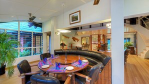 Un espace repas avec une table ronde, des chaises en cuir noir et une vue sur l’extérieur grâce à de grandes fenêtres.