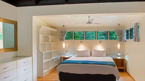 Une chambre à coucher avec un grand lit, des tables de chevet, un ventilateur de plafond et une fenêtre avec des rideaux.