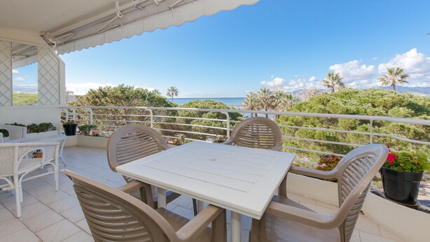 A balcony with a white table and chairs, overlooking a coastal landscape with palm trees and the sea. - Sea View, Cannes Croisette, in Front of the Sea (Cannes)