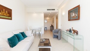 A modern living room with a white sofa, teal cushions, a glass coffee table, a grey armchair, and a glass-top console table with decorative items. - Sea View, Cannes Croisette, in Front of the Sea (Cannes)
