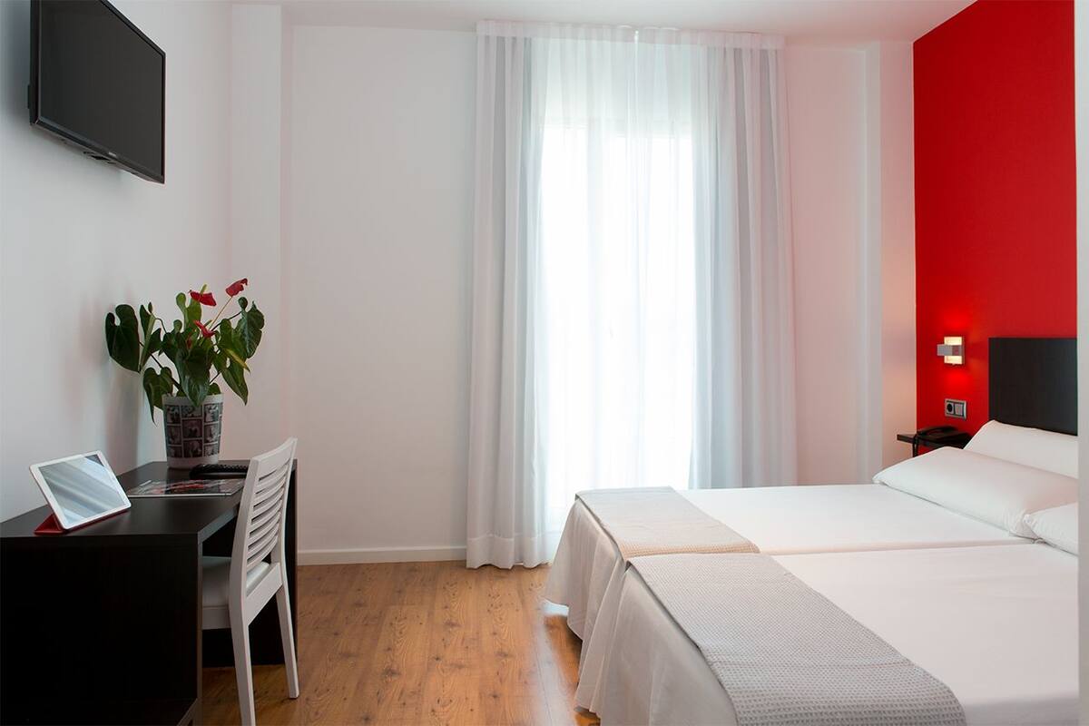 A hotel room with a desk, chair, and a bed.