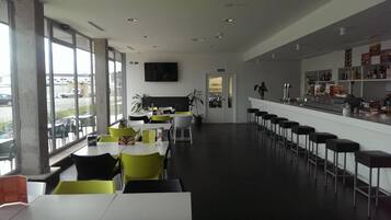 A modern bar area with high stools, a counter with beverages, and a large window overlooking a parking area.