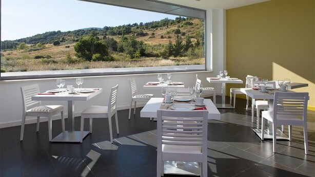A modern dining area with white tables and chairs, large windows offering a view of a hilly landscape. - NRuta Ponferrada (Bembibre)