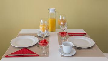 Una preparación para el desayuno que incluye una jarra de jugo de naranja, dos vasos de jugo de naranja, un vaso de agua, un tazón de sandía, una taza blanca y una servilleta roja sobre una mesa.
