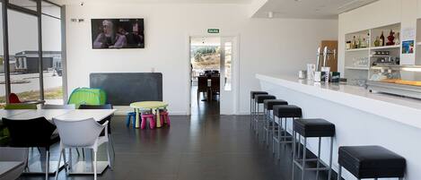 Un espacio de bar moderno con barra, taburetes y una pantalla de televisión que muestra a cocineros.