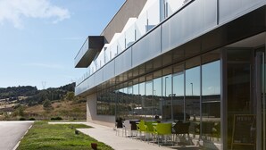 A modern building with a glass facade, outdoor seating area, and a clear view of the surrounding landscape. - NRuta Ponferrada (Bembibre)