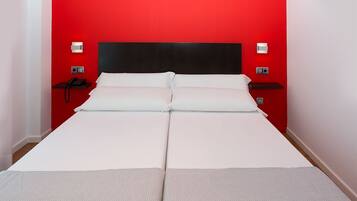 Una cama con cabecera negra y ropa de cama blanca en una habitación con paredes rojas.