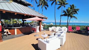A wooden deck with white wicker furniture, a bar area, and a view of the ocean.