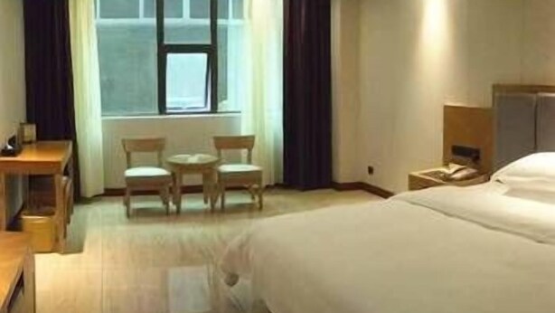 A hotel room with a large bed, a desk with a chair, a small table with two chairs, and a window with curtains. - Chenmao Yuyang Hote (Guigang)