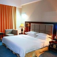 Habitación de hotel con una cama grande, una silla, una mesita de noche con lámpara y un ventanal con cortinas.
