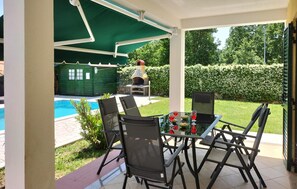 Een terras buiten met een zwembad, een barbecue en een tafel met stoelen.