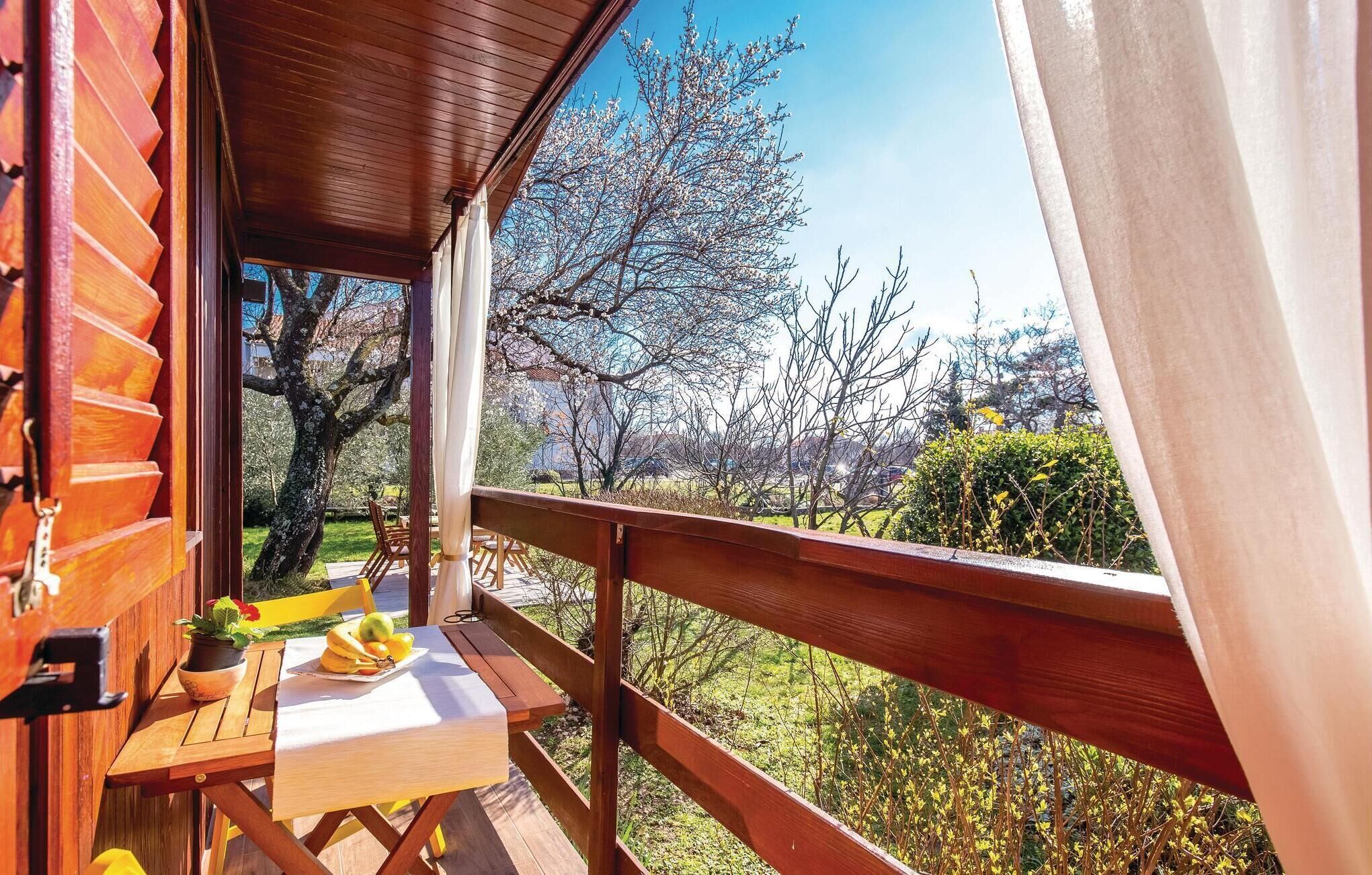 Una terraza de madera con una mesa y sillas, con vista a un jardín con árboles y un cielo despejado.