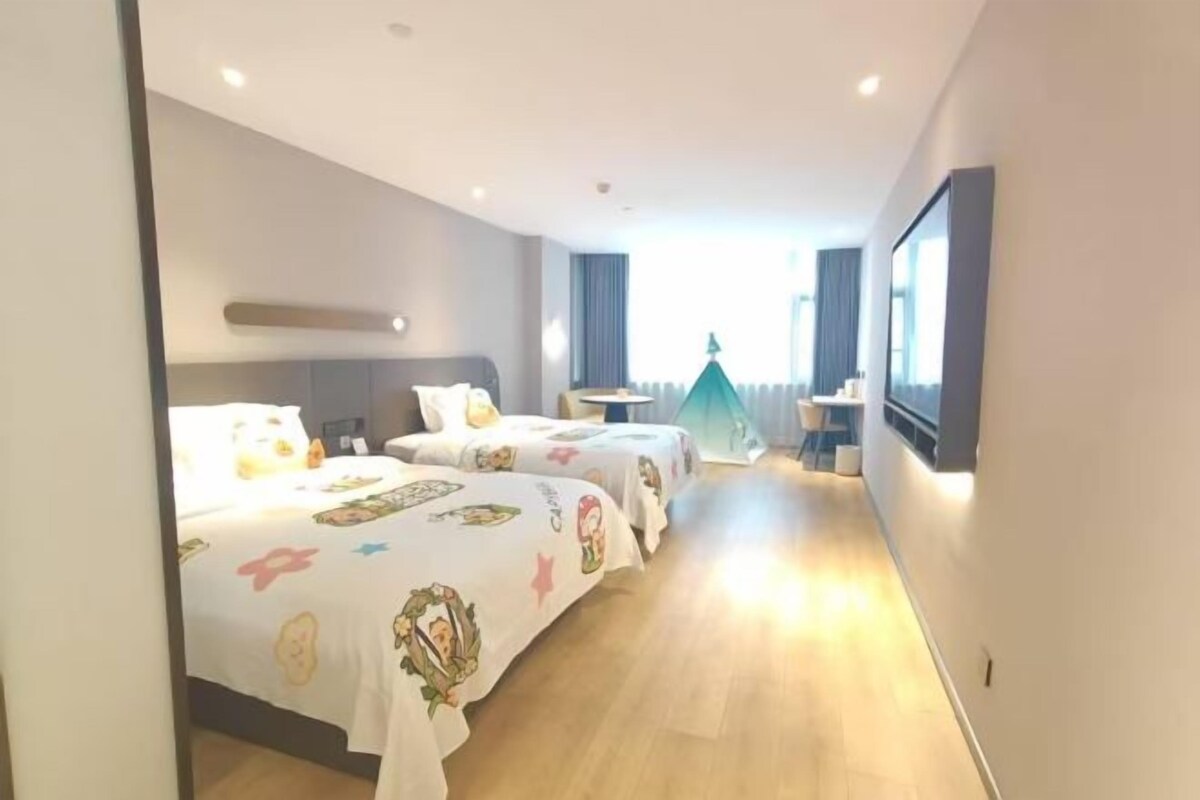A hotel room with two beds, a small table, and a TV mounted on the wall.