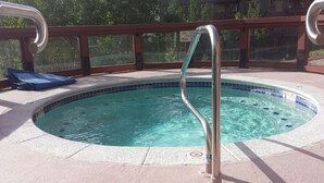 A hot tub with a metal ladder, a blue lounge chair, and a sign indicating spa hours. - Our studio condo is the closest condo to the Eagle Lift.  Just steps away. (Frisco)