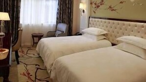 A hotel room with two beds, a chair, a lamp, and a painting on the wall. - Modern Square Hotel (Lishui)