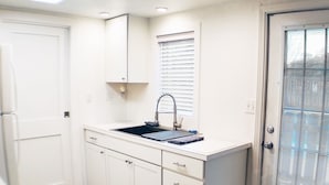 A small kitchen with white cabinets, a sink, and a window with blinds.