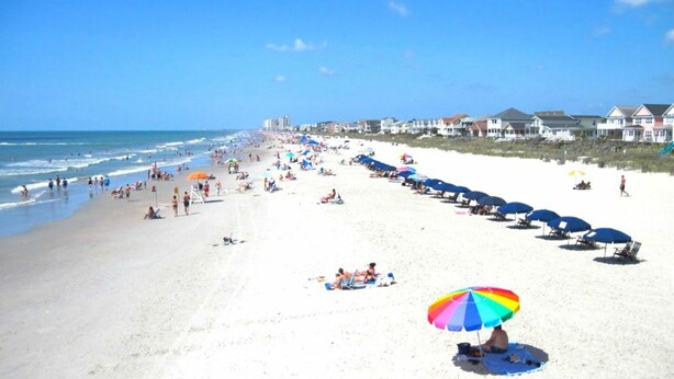 A beach with rows of beach umbrellas and people sunbathing.