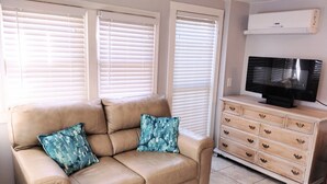 A beige leather sofa with two patterned cushions, a wooden dresser with multiple drawers, and a television on top.