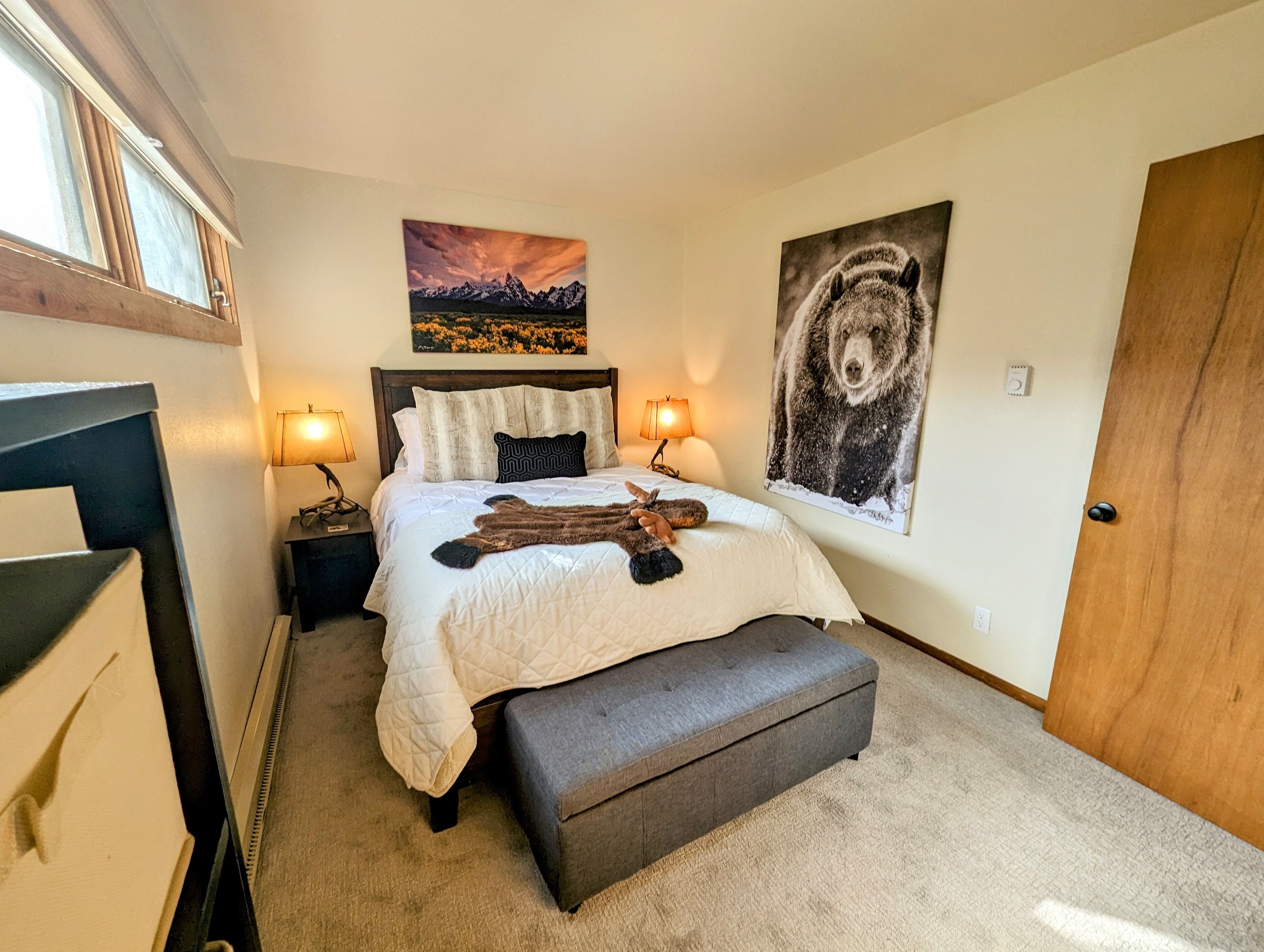 Une chambre à coucher avec un lit, des lampes de chevet, un banc, un tableau représentant un ours et un paysage de montagne.