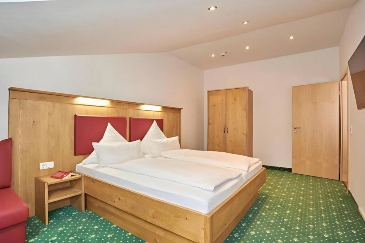 A room with a wooden bed, a red chair, a wardrobe, and a small table.