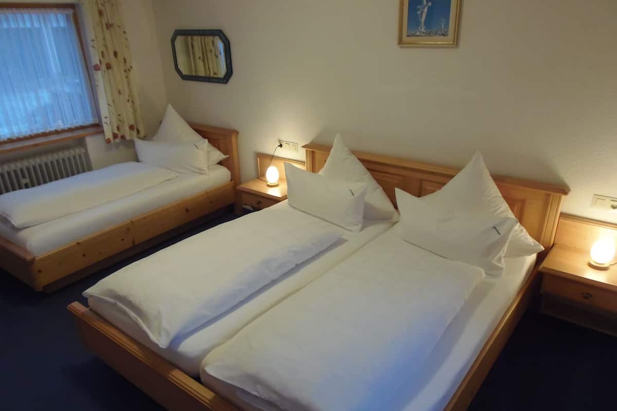 Duas camas de solteiro com estrutura de madeira e roupa de cama branca, cada uma com mesa de cabeceira e abajur.