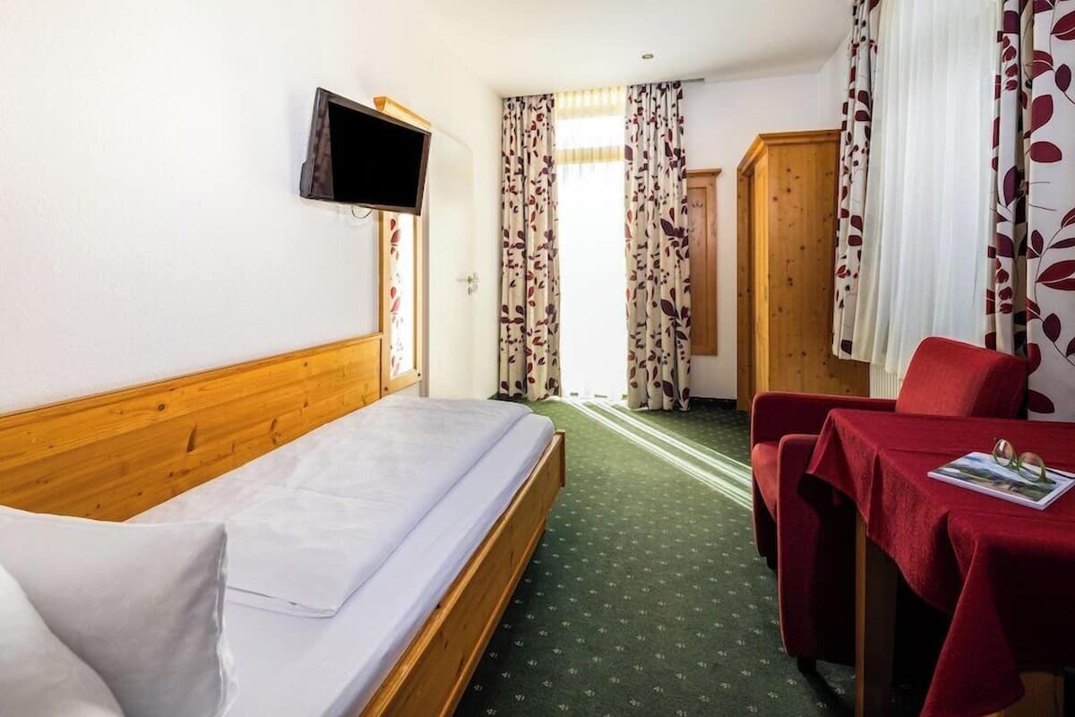 Quarto de hotel com uma cama, televisão na parede, secretária com mesa e uma cadeira.