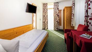 A hotel room with a bed, a TV mounted on the wall, a desk with a table, and a chair.